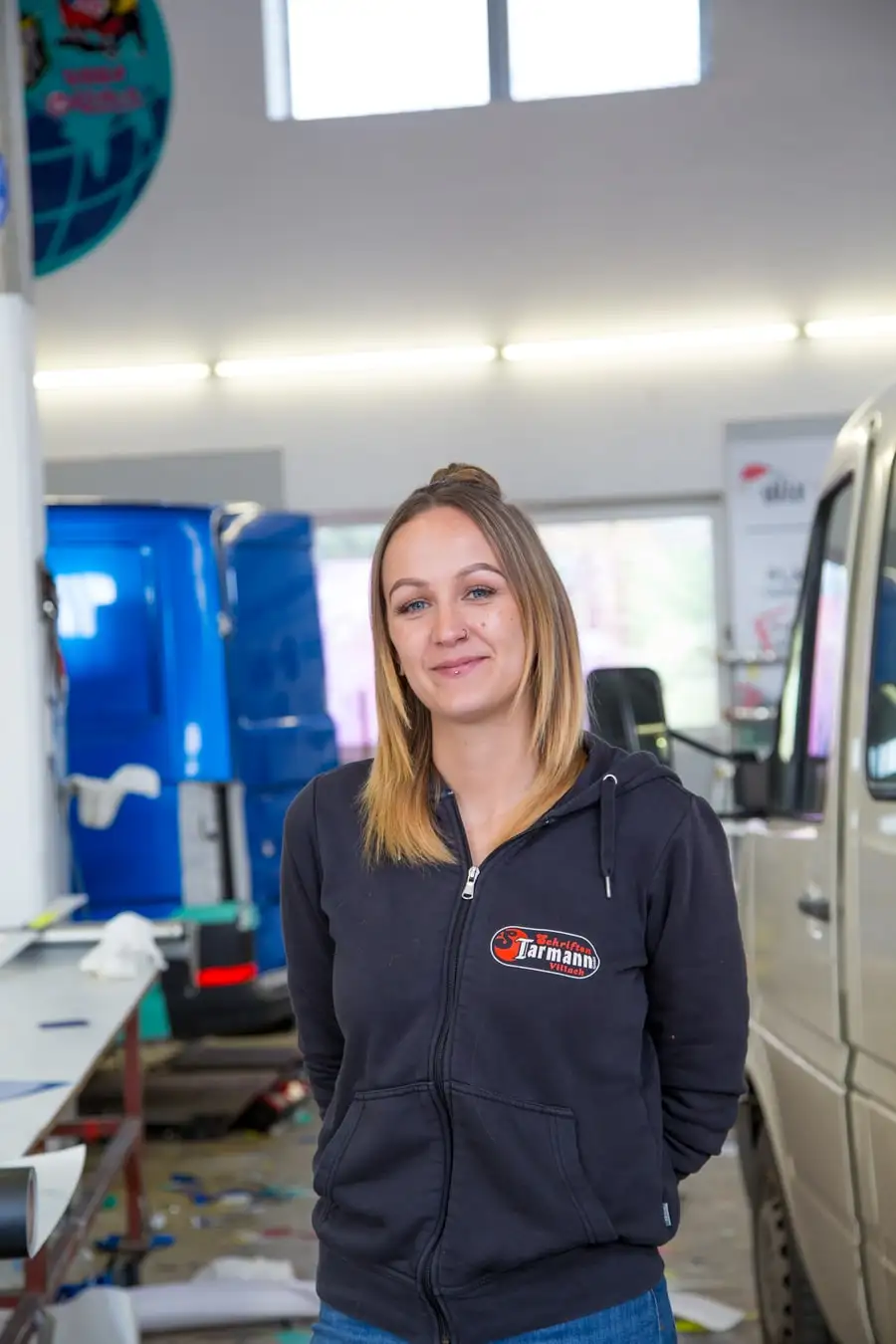 Porträt von Christin Schorn in Firmenjacke in der Werkstatt von Schriften Tarmann