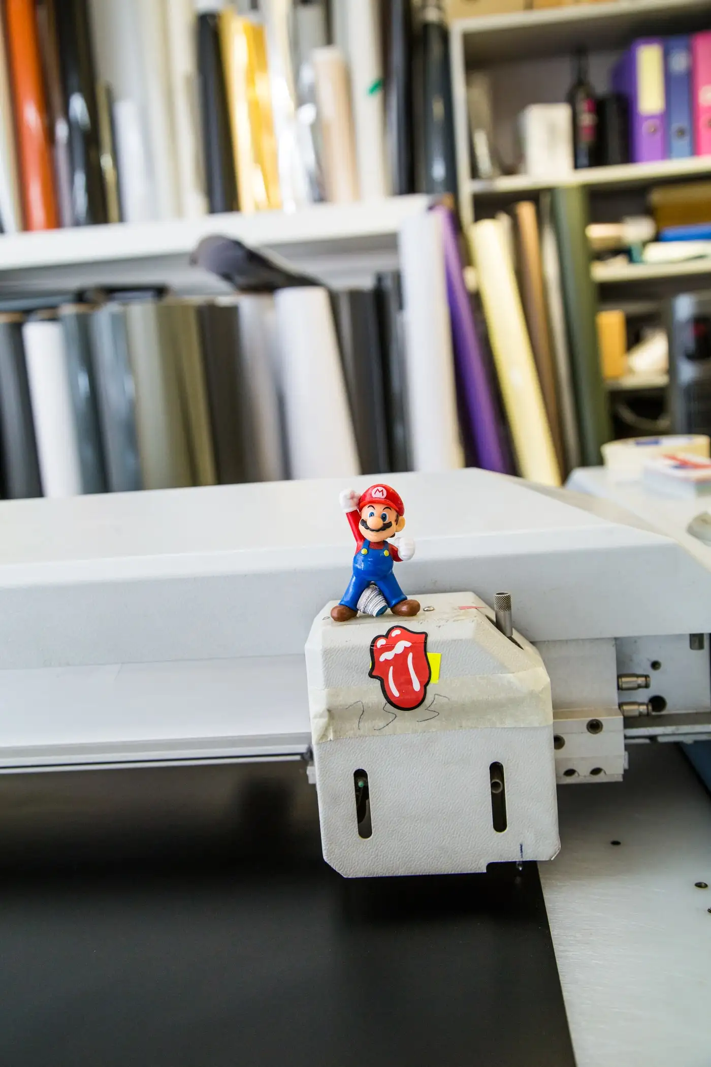 Flachbett-Schneidetisch in der Werkstatt, dahinter ein Regal mit Folienrollen