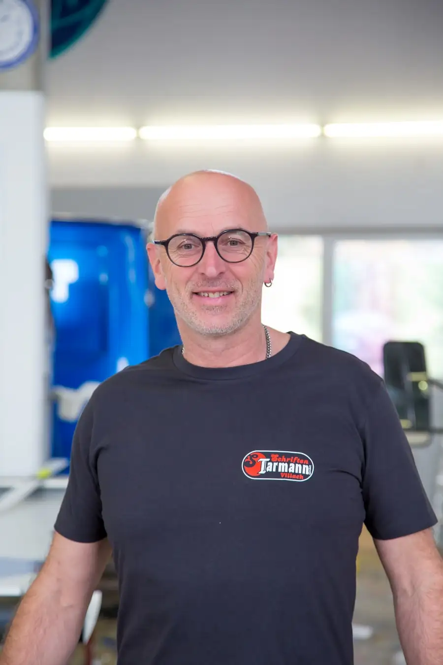 Porträt von Franz Öhlweiner im Firmen-T-Shirt vor einem Fahrzeug in der Werkstatt