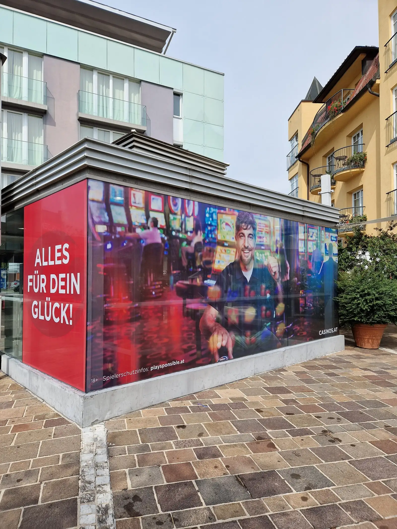 Glaspavillon, vollflächig mit rot bedruckter Folie beklebt, im öffentlichen Raum