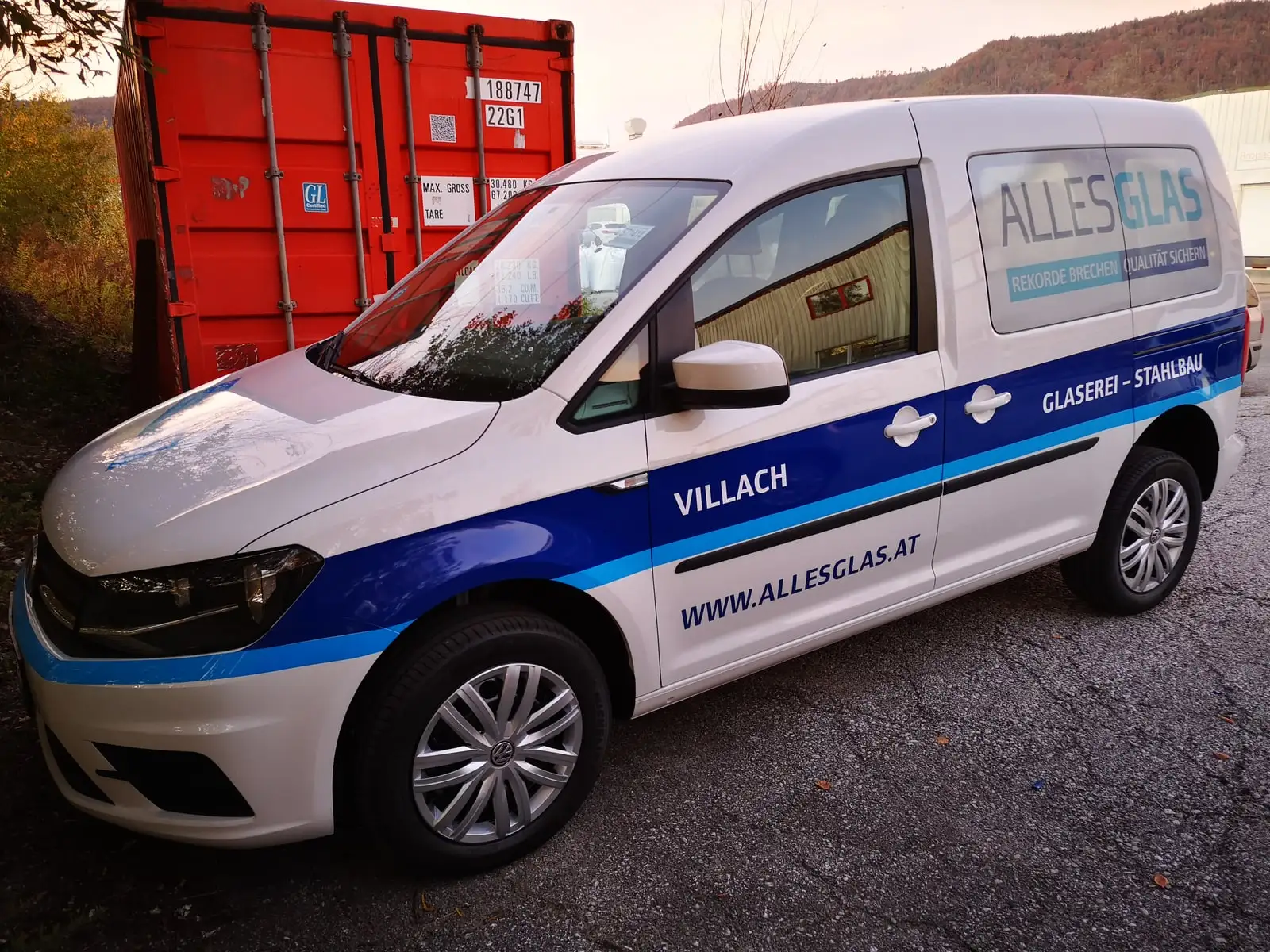 Weißer Hochdachkombi mit blauer Firmenbeschriftung im Freien