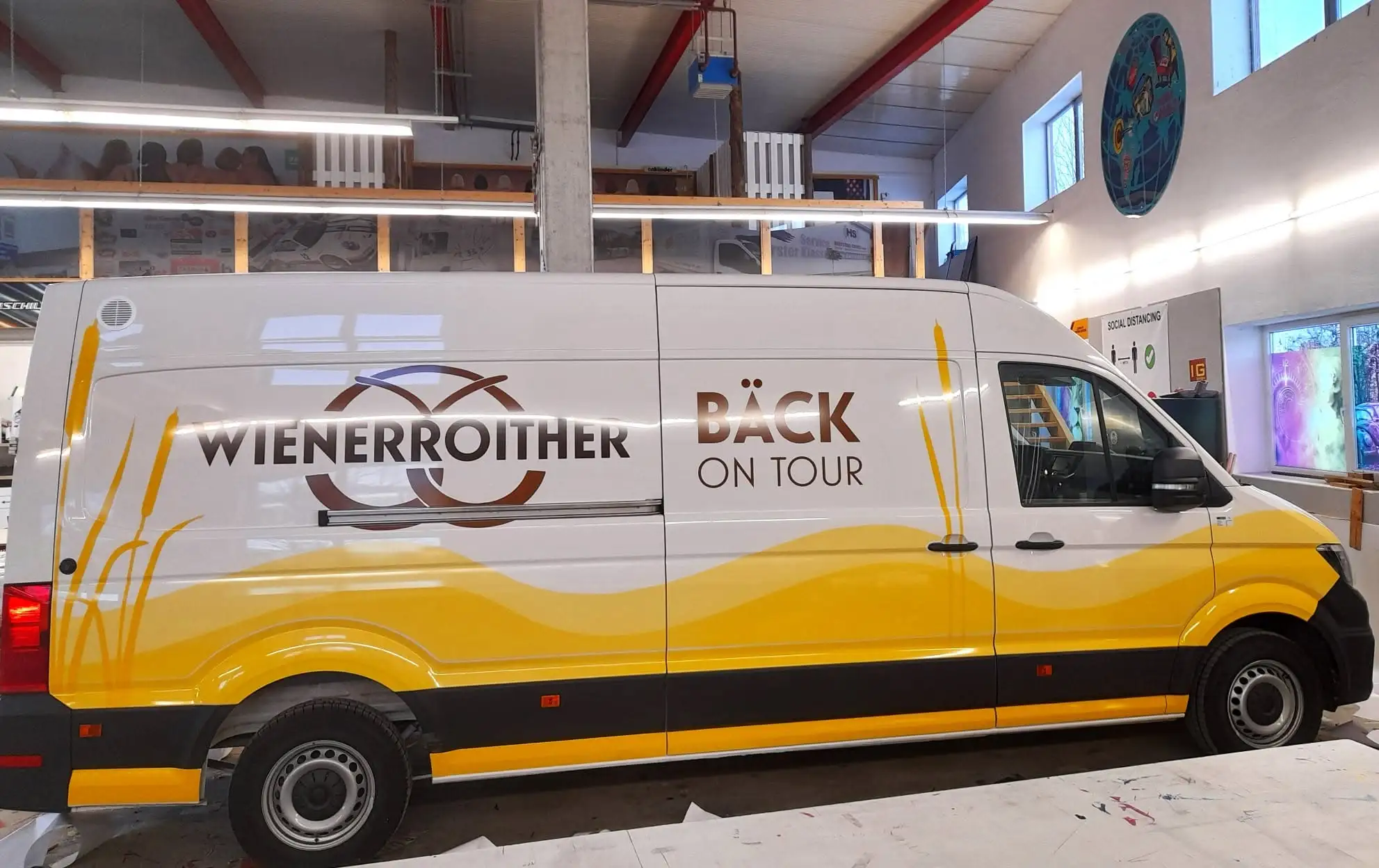 Weiß-gelber Kastenwagen mit großem braunem Logo und Schriftzug an der Seite in der Werkstatt