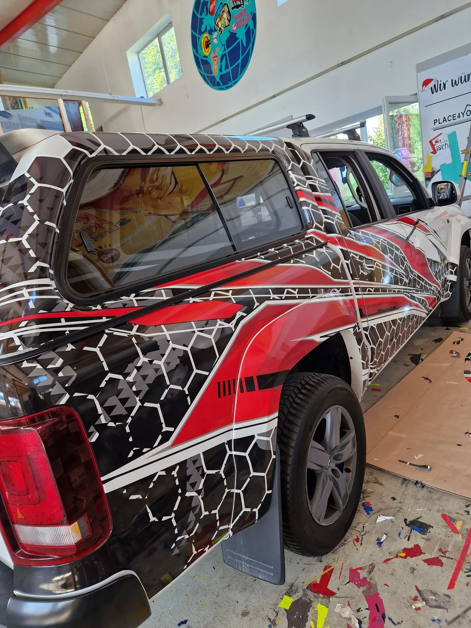 Pick-up mit Hardtop und rot-schwarz-weißem Wrap in der Werkstatt, am Boden Folienverschnitt