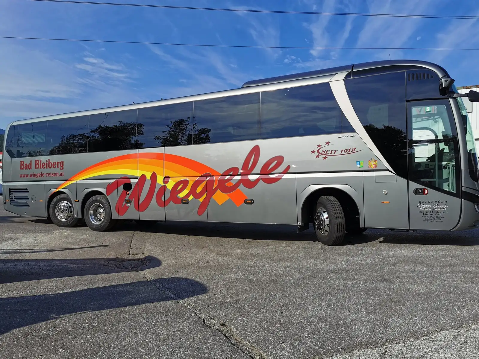 Silbergrauer Reisebus mit großflächigem Schriftzug und farbigem Schwung auf der Seite