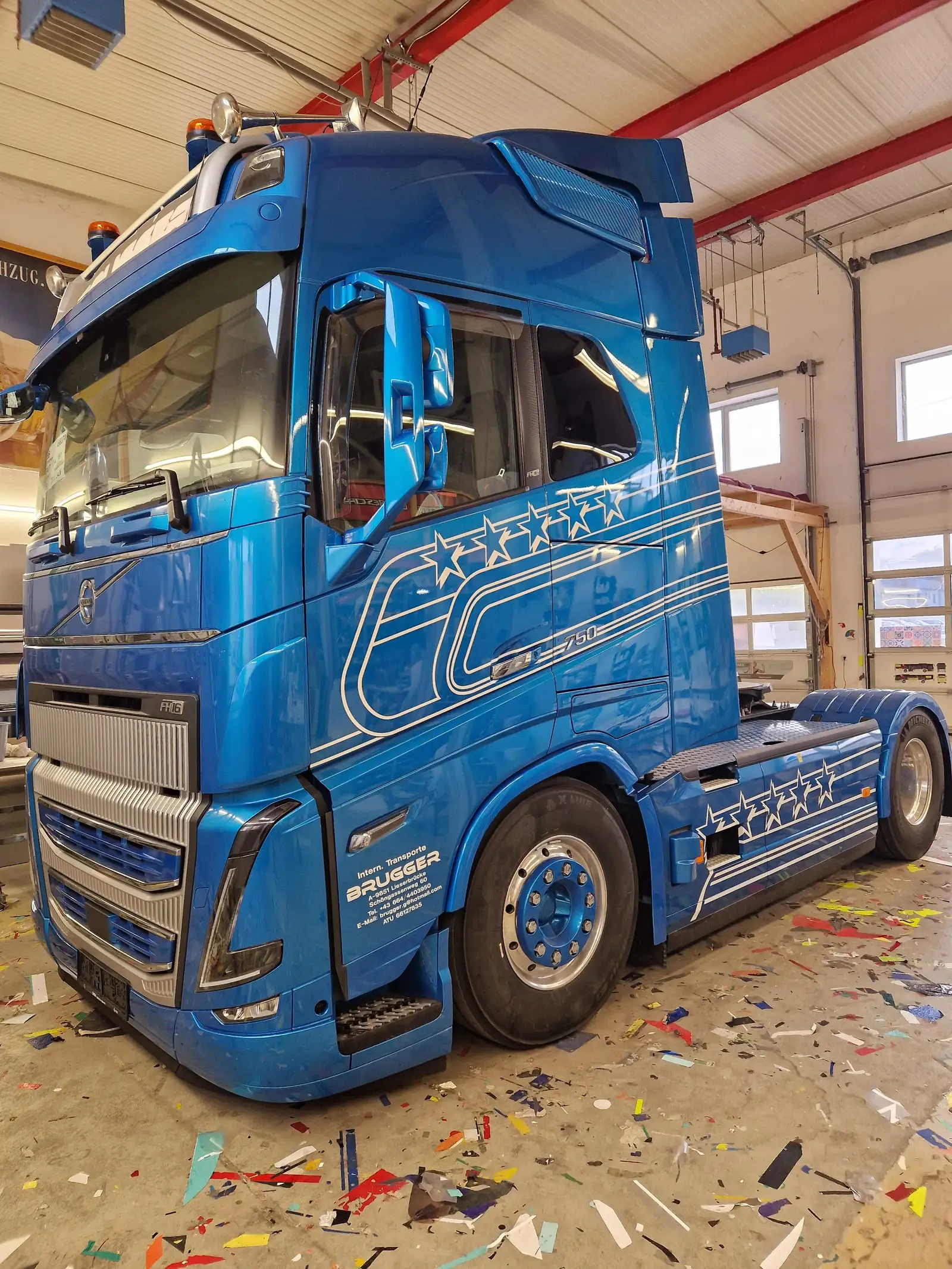 Blaue Sattelzugmaschine mit silbernen Linien- und Sterndekoren in der Werkstatthalle